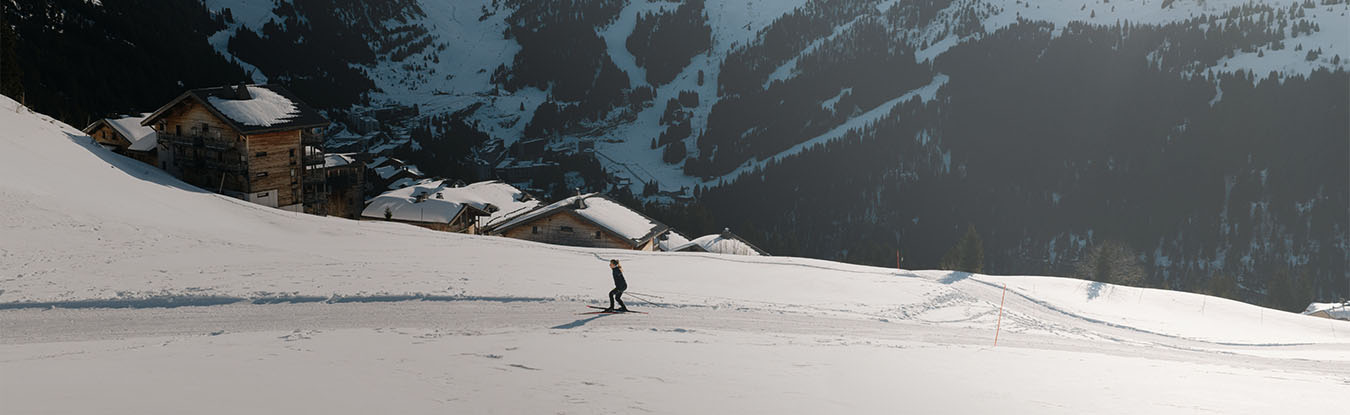 A cross-country skiing session at Col de Pierre Carrée, Flaine. The shot captures a skier in full effort on a snowy trail, lined with traditional chalets against the backdrop of the rugged Haute-Savoie mountains.